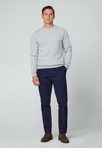 Grauer Sweatshirt mit Rundhalsausschnitt, gerippten Bündchen und Taillenbund. Kombiniert mit dunkelblauen Hosen und braunen Schnürschuhen.