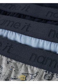 Trzy pary chłopięcej bielizny z gumkami w pasie. Kolory to granatowy, jasnoniebieski i szary z nadrukiem graficznym. Materiał wydaje się miękki i elastyczny.