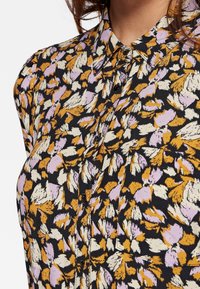 Camicia con motivo floreale nera, con accenti viola, arancioni e crema. Tessuto leggero con colletto classico e chiusura con bottoni.