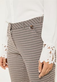 Hnědo-bílé kostkované kalhoty s těsným střihem. Obsahují hnědý knoflík a jako ozdobu krajku na bílých rukávech.