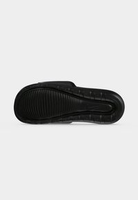 Μαύρη σόλα σανδάλιου Nike slide με υφή και ανάγλυφο λογότυπο Nike swoosh σε μονόχρωμο γκρι φόντο.