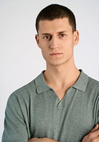 Ljusgrön pikétröja med korta ärmar och pikékrage, tillverkad av ett mjukt, texturerat material. Har ett subtilt ribbat mönster och en figurnära passform.