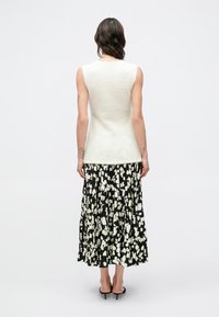 Stickad, ärmlös top i gräddvit färg kombinerad med en svart, plisserad maxikjol med vitt blommönster. Mjuk textur, figurnära silhuett och minimalistisk design.