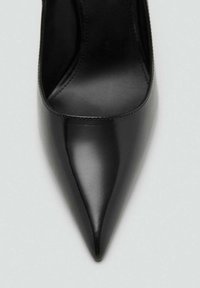 Zapatos de tacón negro con punta afilada, hechos de cuero suave. Cuentan con un acabado brillante y elegante, con un diseño sencillo y costuras mínimas.