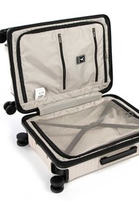 Valigia rigida di colore crema con accenti neri. Presenta un interno con zip, scomparti e tasche in rete. Quattro ruote girevoli.