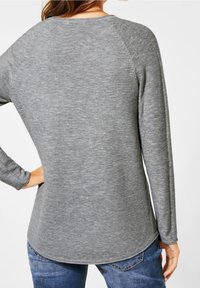 Haut gris à manches longues avec une texture côtelée, présentant un ourlet arrondi et des manches raglan. Associé à un jean bleu, vu de dos.