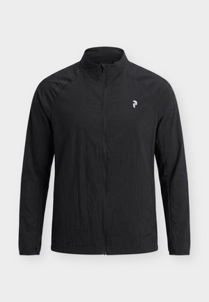 Schwarze leichte Jacke mit durchgehendem Reißverschluss, langen Ärmeln und kleinem weißem geometrischen Logo auf der linken Brust vor einfarbigem Hintergrund.