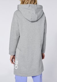 Felpa grigia con cappuccio e maniche lunghe, caratterizzata da un logo laterale bianco. Tessuto morbido e texture, con una vestibilità rilassata e lunghezza intermedia.