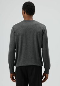 Donkergrijze trui met lange mouwen, ronde hals en een gladde textuur. Heeft geribde manchetten en boord, gedragen over een donkere broek.