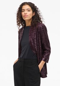 Särav tumelilla litritega jakk kolmveerandvarrukatega, ees avatud, kantud musta topi peal ja sobitatud mustade pükstega.