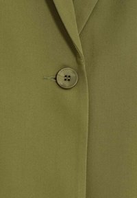 Blazer verde oliva con una tela texturizada, que presenta un cierre de un solo botón y solapas bien estructuradas.
