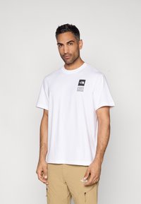 Λευκό βαμβακερό T-shirt με άνετη εφαρμογή, που διαθέτει μαύρο σήμα λογότυπου στο αριστερό στήθος. Κοντά μανίκια και στρογγυλή λαιμόκοψη. Απλός σχεδιασμός.