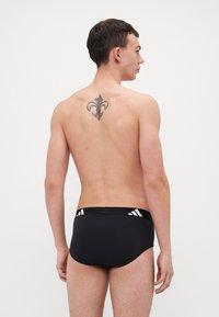 Schwarze Badehosen im engen Design, mit einem kontrastierenden schwarz-weißen elastischen Bund, der ein Logo und dekorative Akzente aufweist.