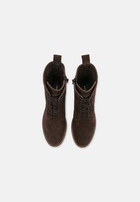 Stivali alla caviglia in suede marrone con lacci frontali, linguette per il trascinamento e cuciture a contrasto. Suole piatte e stivali alti offrono supporto e copertura.