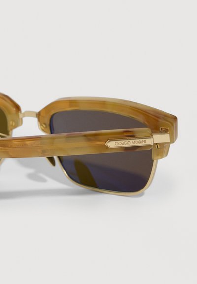 Saules brilles ar caurspīdīgām dzintara taisnstūra rāmjiem un tumšiem objektīviem, ar zelta "Giorgio Armani" logotipa plāksni uz tempļa roktura.