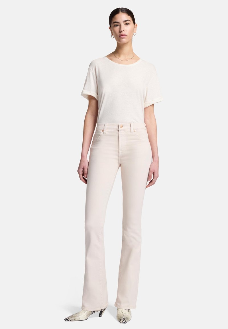 Jean évasé beige clair associé à un t-shirt à manches courtes couleur crème. Tissu texturé avec des manches retroussées. Les chaussures présentent un motif reptile.