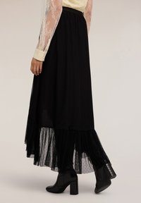 Gonna nera con orlo in tulle a strati con pois. Design fluido con vita aderente, abbinata a stivali neri con tacco.