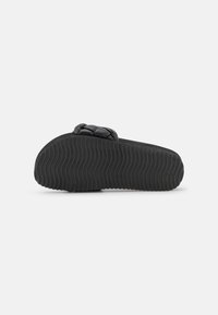 Black slide sandal with a textured rubber sole, featuring a braided strap design. Smooth upper material, low-profile shape, and flexible construction.