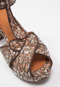 Sandale à talon haut marron à motif, présentant un bout ouvert, un matériau texturé et une garniture contrastante. La semelle est en cuir marron doux.