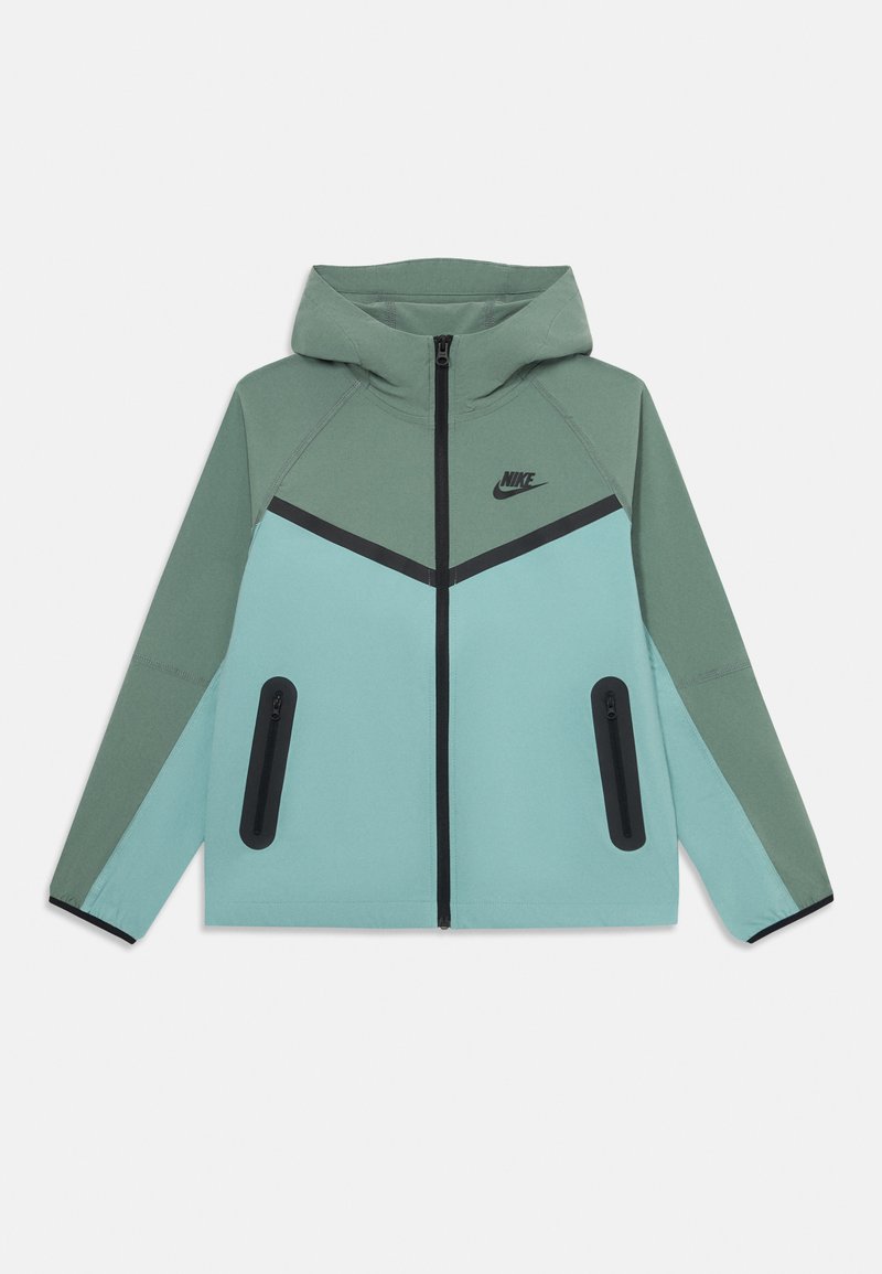 Nike džemperis su dviejų tonų žaliais ir šviesiai mėlynais paneliais, juodu užtrauktuku, užtrauktukais uždaromomis kišenėmis ir Nike logotipu ant krūtinės, išdėtas ant baltos fono.
