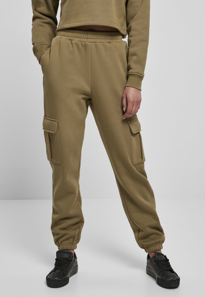 Personne portant un jogger cargo vert olive avec une ceinture élastique et des poignets, des baskets noires, et un sweat-shirt assorti raccourci, debout les mains dans les poches.