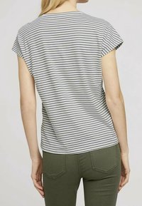 Camiseta de manga corta a rayas grises y blancas con un corte relajado, vista desde la espalda, combinada con pantalones ajustados de color verde oscuro.