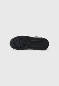 Soletta di sneaker nera con gomma testurizzata e motivi circolari e lineari. Il marchio "JORDAN" è impresso vicino al tallone.