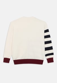 Κρεμ πλεκτό πουλόβερ με μπορντό ριμπ τελείωμα, που διαθέτει ριγέ μανίκι σε ναυτικό μπλε και άσπρο. Απλός, κλασικός σχεδιασμός χωρίς επιπλέον διακοσμητικά.