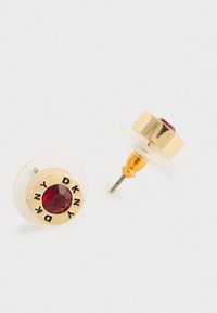 Orecchini a bottone in oro con centri in pietra preziosa rossa, logo DKNY inciso attorno alle pietre e supporti in plastica trasparente su fondo bianco.