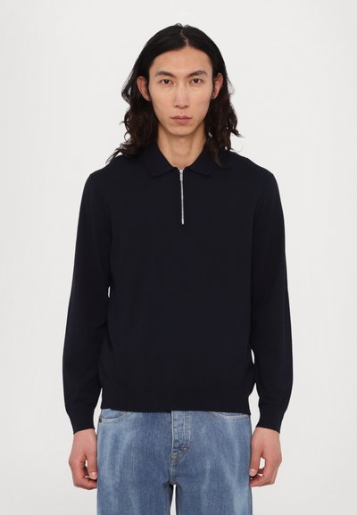 Pull en maille bleu marine foncé à manches longues, avec une ouverture zippée au niveau du cou et une texture côtelée discrète aux poignets et à l'ourlet.
