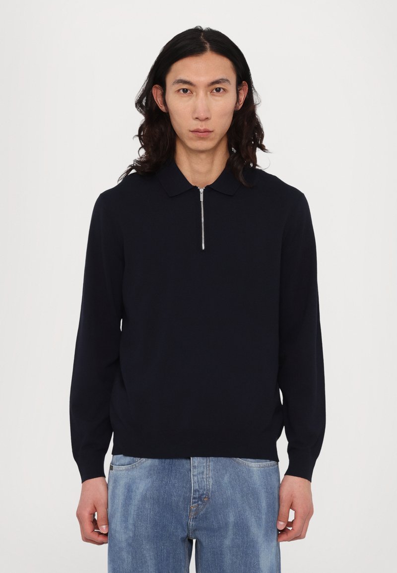 Sötét tengerészkék kötött póló pulóver hosszú ujjakkal, zipzáras nyakkivágással és finom bordázott textúrával az ujjak végén és az alján.