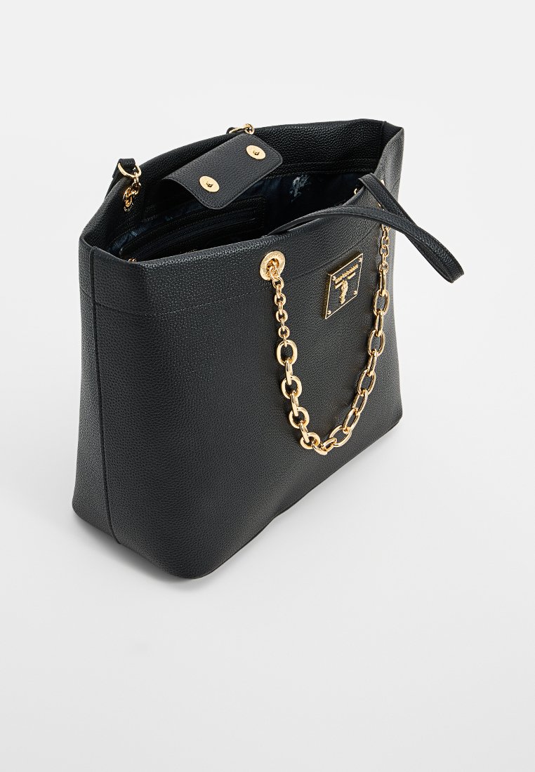 Sac fourre-tout en cuir noir texturé avec une poignée en chaîne dorée, fermeture à rabat supérieure et accents en matériel doré. L'intérieur comprend des poches pour l'organisation.