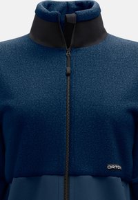 Marineblaues Fleece-Jacke mit hohem Kragen, ausgestattet mit einem Reißverschluss vorne und einem glatten schwarzen Paneel. Logosticker nahe dem Saum, strukturierten Stoff.