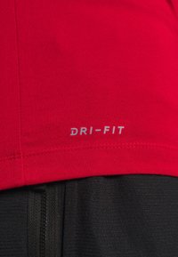 Rode Dri-Fit sportshirt met een gladde textuur, korte mouwen en een lichtgrijs logo op de zoom. Gecombineerd met zwarte gestructureerde stof.