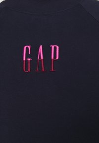 Laivastonsininen collegepaita, jossa on "GAP"-logo vaaleanpunaisella kirjailulla. Kirjaimissa on liukuvärjäys, joka siirtyy kirkkaasta tummaan vaaleanpunaiseen.