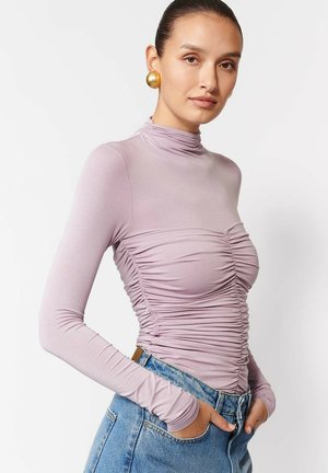 Fioletowa bluzka z długim rękawem i stójką, z marszczeniami po bokach, w połączeniu z niebieskimi jeansami o wysokim stanie.