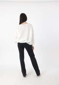 Witte, gebreide trui met een losse pasvorm en verlaagde schouders, gecombineerd met zwarte, rechte jeans. Minimalistisch ontwerp met een zachte textuur.