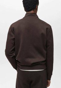 Giacca felpa marrone con colletto alto, realizzata in tessuto morbido, con una vestibilità rilassata e polsini e orlo a costine.