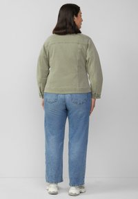 Olivgrüne Jeansjacke mit tailliertem Design, geraden Rückennähten und langen Ärmeln, kombiniert mit hellblauen, geraden Jeans.