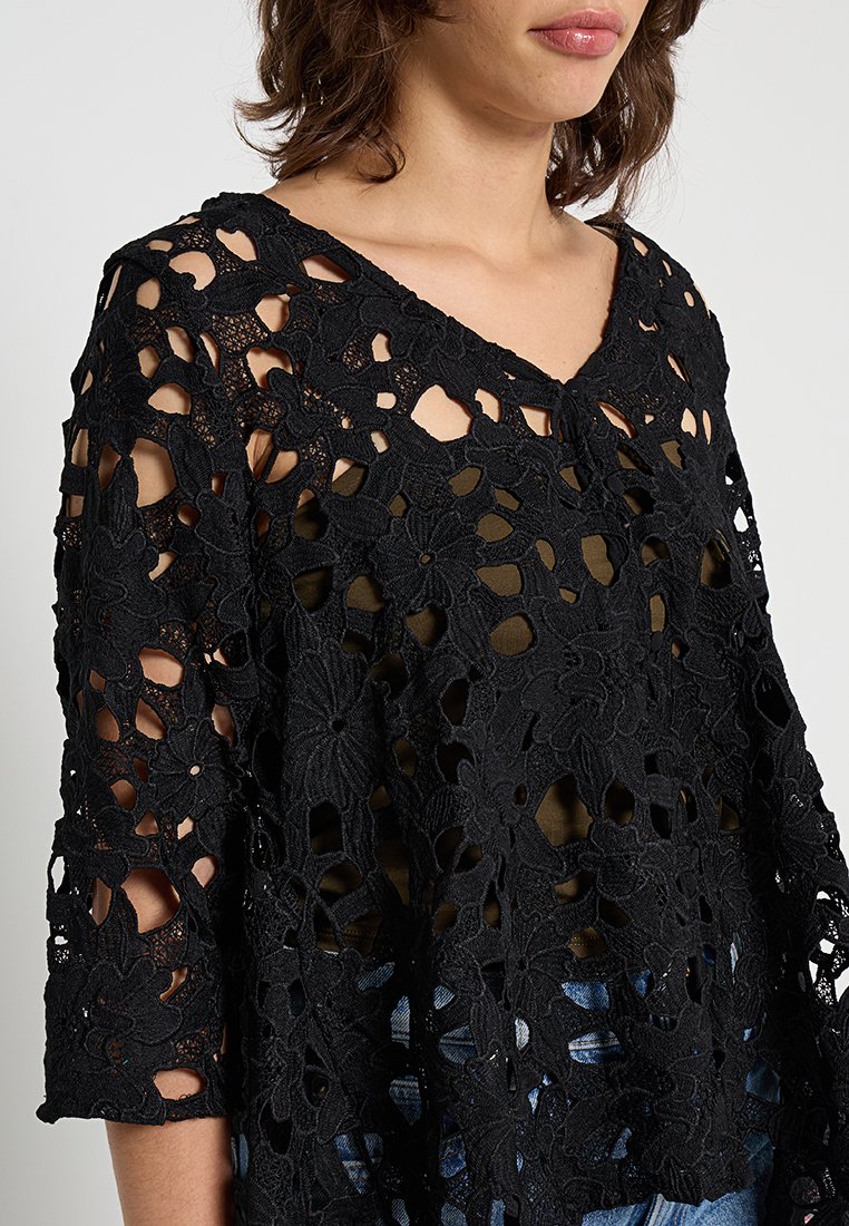 Schwarzes Spitzenoberteil mit floralem Cut-Out, V-Ausschnitt und Dreiviertelärmeln. Der Stoff ist leicht und luftig und lässt einen Hauch der darunterliegenden Schicht durchscheinen.