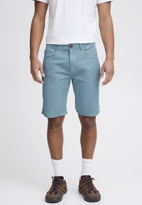 Lys blå shorts med slim fit, synlige forlommer og brun knaplukning, parret med mørkebrune sneakers og hvide strømper.