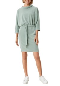 Minttu vihreä mekko, jossa on kaula-aukko, kolmivartiset hihat, säädettävä sidontavyö ja sileä rakenne. Yhdistetty valkoisiin lenkkareihin.