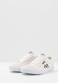Canvas-sneakers i krämfärg med ett svart rutmönster på sidan, vita accenter och vita snörningar. Platt gummisula för bra grepp.
