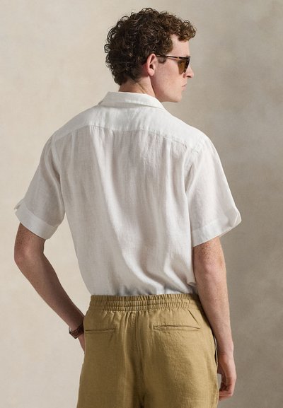 Chemise à manches courtes en lin de couleur claire, coupe décontractée, associée à un short à taille élastique marron clair avec poches arrière. Texture lisse.