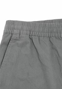 Pantalon en tissu gris avec une ceinture élastique et des coutures visibles sur les poches latérales, montré en gros plan.