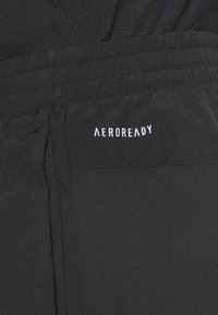 Pantalones cortos deportivos negros con una textura suave y una cinturilla fruncida. Presenta el logo "AEROREADY" en blanco en el lado.