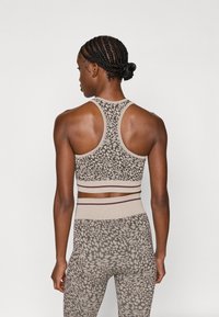 Sportlik komplekt, mis sisaldab beeži lühikest tanki, millel on leopardimuster, ja sobivaid kõrge vöökohaga pükse kontrastsete triipudega.