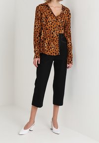 Blusa con stampa animale marrone e nera, maniche lunghe, scollatura a v, abbinata a pantaloni cropped neri e décolleté bianchi con tacco.