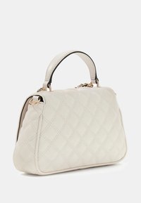 Sac à main blanc matelassé de forme arrondie, en cuir, avec des accents métalliques dorés et une poignée bordée de noir.
