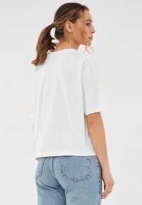 T-shirt en coton blanc avec une coupe détendue, des épaules tombantes et un col arrondi. Associé à un jean en denim bleu clair, avec des poches arrière.